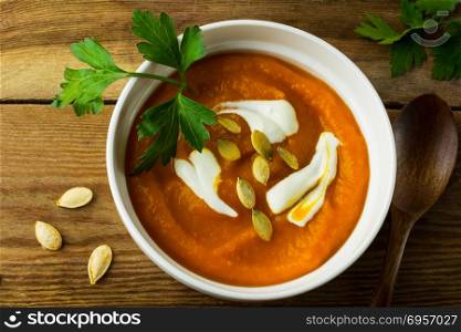 Roasted pumpkin squash cream soup with cream and pumpkin seeds in the white bowl on the dark wooden background, top view. Pumpkin soup on the dark wooden background