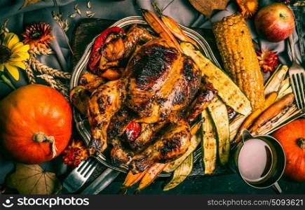 Roasted stuffed whole turkey or chicken with organic harvest vegetables and pumpkin for Thanksgiving dinner served on rustic table with fall flowers arrangements, top view