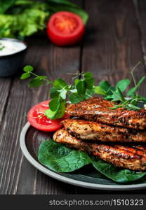 Roasted turkey fillet with bright appetizing fried crust with spices and spring herbs on a black plate, old dark wooden table. Rustic style, close-up.