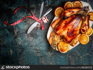 Roasted turkey or chicken with orange slices in plate for Christmas dinner served with fork,knife and festive decoration on dark rustic background, top view
