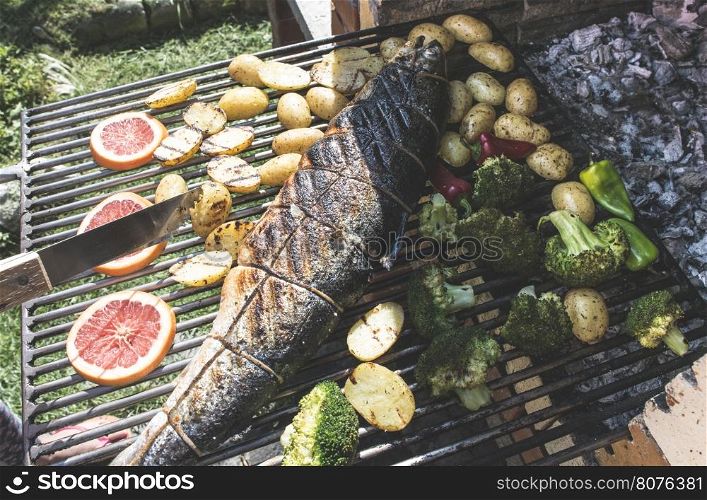 Roasting salmon fish on grill. Vegetables on grill in a garden