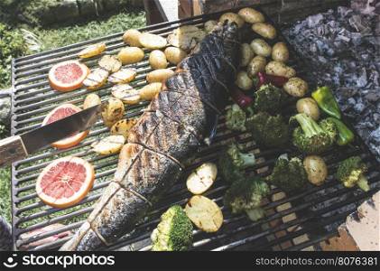 Roasting salmon fish on grill. Vegetables on grill in a garden