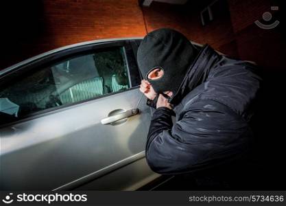 Robber and the car thief in a mask opens the door of the car and hijacks the car.