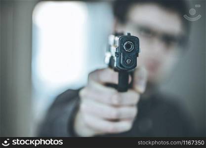 Robber or criminal is aiming with a black gun, blurry face