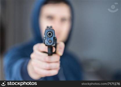Robber or criminal is aiming with a black gun, blurry face