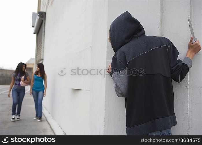 Robber with knife hiding behind corner and waiting for two girls