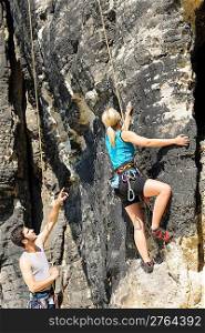Rock climbing male instructor hold rope blond woman sunny day