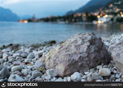Rock in the foreground, cute little Italian village with lights in the background. Evening.
