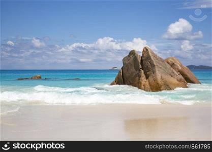 Rock juts out of waves on the white beach of Seychelles