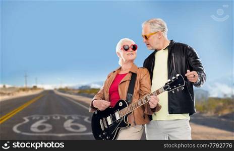 rock music, old age and travel concept - happy senior couple with electric guitar over us route 66 background. senior couple with electric guitar over route 66