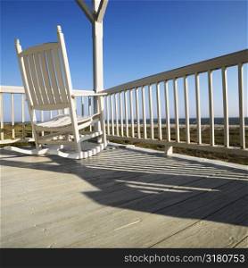 Rocking chair on porch with railing overlooking beach at Bald Head Island, North Carolina.