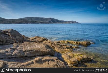 Rocks and sea overlooking La Revellata lighthouse near Calvi in Corsica with blue skies and blue sea