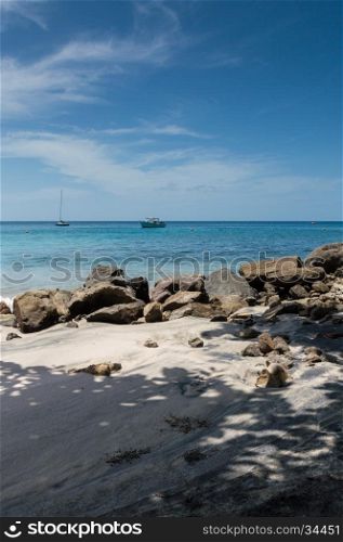 Rocks and shadows on the beach with boats on the sea beyond, in Saint Lucia