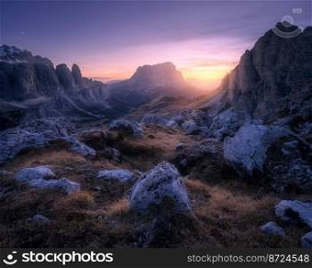 Rocks and stones at colorful sunset in autumn in Dolomites, Italy. Landscape with mountains, trail, hill, orange grass and trees, purple sky with clouds in fall at night. Hiking in mountains. Dusk. Rocks and stones at colorful sunset in autumn in Dolomites, Italy