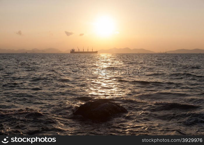 Rocks beach side In the morning the sun rises. And behind a large cargo ship.