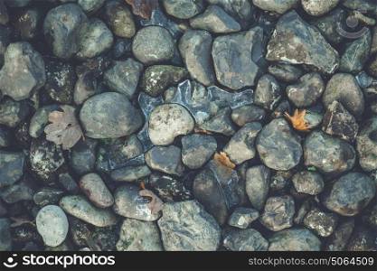 Rocks in a pile in the winter with ice and leaves between the pebbles in a natural pattern