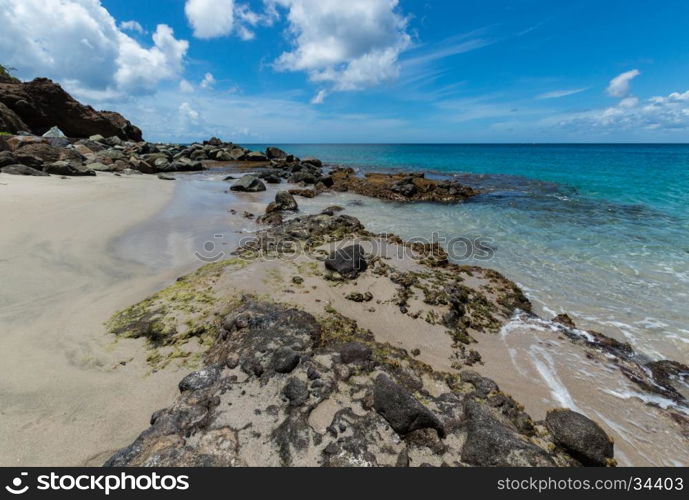 Rocks in the sand at the edge of the clear blue sea in Saint Lucia