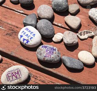 Rocks with writing and drawings are scattered across a red picnic table as they are being used in a family art project.