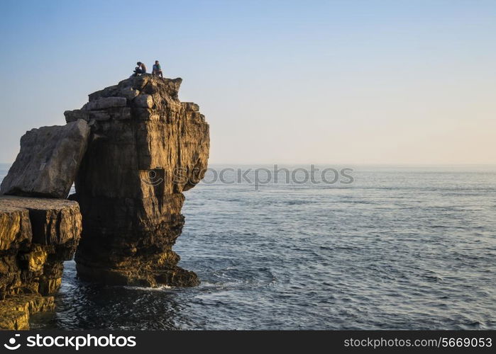 Rocky cliff landscape with sunset over ocean with undientified people on cliff top