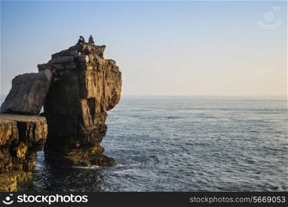 Rocky cliff landscape with sunset over ocean with undientified people on cliff top