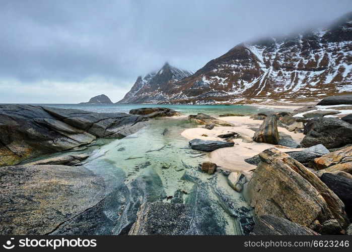 Rocky coast of fjord of Norwegian sea in winter with snow. Haukland beach, Lofoten islands, Norway. Rocky coast of fjord in Norway