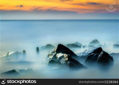 Rocky coast of sea. Slow shutter speed for smooth water level and dreamy effect. Seascape, water rolling over rocks at coastline mist long exposure scenic background.