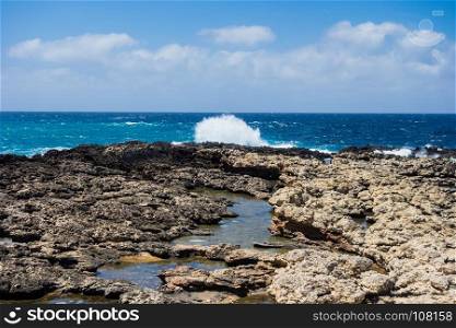 Rocky coastline and tide pools with splashing waves under partly cloudy sky in Malta.