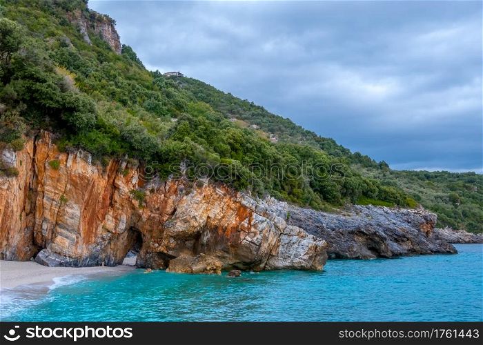 Rocky forest shore of the sea in cloudy weather. Villa on the slope. There is a natural stone arch on the beach. Rocky Forest Shore of the Sea