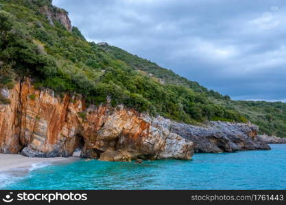 Rocky forest shore of the sea in cloudy weather. Villa on the slope. There is a natural stone arch on the beach. Rocky Forest Shore of the Sea