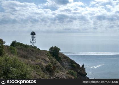 Rocky seashore view with calm sea cloudy sky and watchtower on cliff