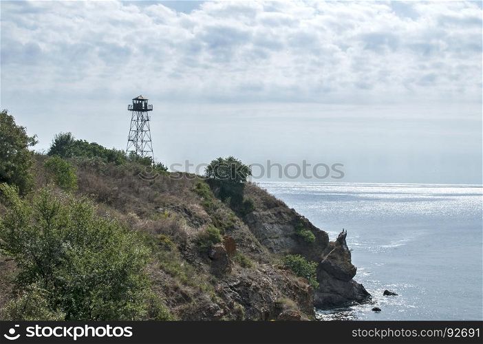 Rocky seashore view with calm sea cloudy sky and watchtower on cliff