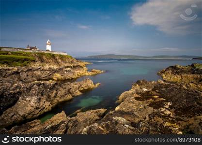 rocky shoreline with turquoise pools and the historic Broadhaven Lighthouse on a clifftop promontory at the entrance of Broadhaven Bay