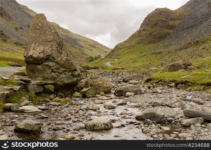 Rocky stream runs by steep road in Honister Pass in English Lake District
