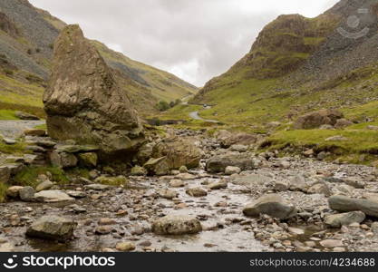 Rocky stream runs by steep road in Honister Pass in English Lake District