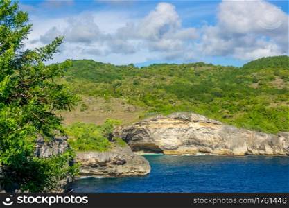 Rocky tropical coast in sunny day. Clouds in the blue sky. Palm trees and green vegetation. Rocky Tropical Coast in Sunny Day