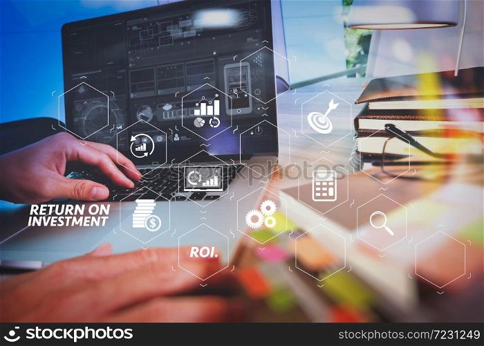 ROI Return on Investment indicator in virtual dashboard for improving business. Designer hand working with laptop computer and smart phone on wooden desk as responsive web design concept