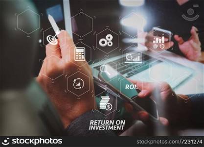 ROI Return on Investment indicator in virtual dashboard for improving business. website graphic designer hand working with his team make new project in studio.Modern laptop extend screen digital tablet smart phone.