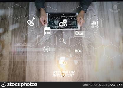 ROI Return on Investment indicator in virtual dashboard for improving business. Creative business working. Photo graphic designer hand working with design digital tablet and ligt bulb on wood table.