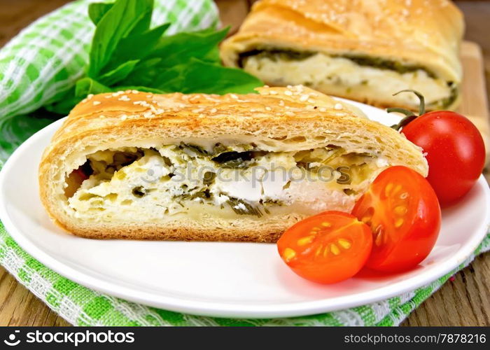 Roll layered with spinach and cheese, tomatoes in a bowl, green napkin on a wooden boards background