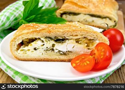 Roll layered with spinach and cheese, tomatoes in a bowl, green napkin on a wooden boards background