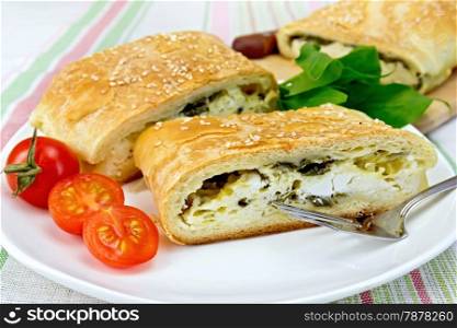 Roll layered with spinach and cheese, tomatoes, spinach leaves in a bowl on a background of a linen tablecloth