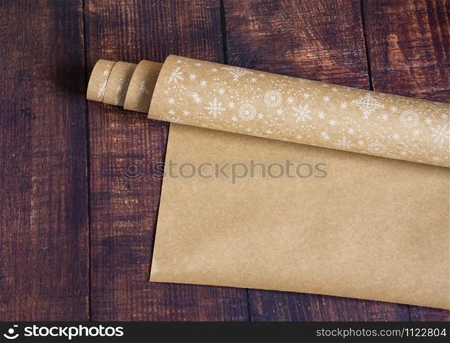 Roll of brown kraft paper with a pattern of snowflakes on a wooden background. Eco paper. Secondary, environmentally friendly. Material for package packaging. Kraft paper for gift wrapping.. Roll of brown kraft paper with a pattern of snowflakes on a wooden background. Eco paper. Secondary, environmentally friendly. Material for package packaging. Gift wrapping paper.