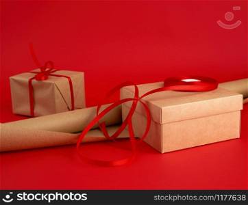 roll of brown paper for packaging, a reel of red ribbon and a wrapped gift in brown kraft paper on a red background, making surprises