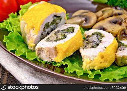 Roll of chicken breast with spinach, mushrooms and cheese in a brown plate with fried mushrooms on a green lettuce, a napkin, tomatoes on a wooden boards background