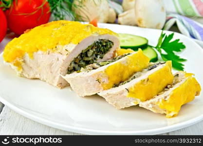 Roll of chicken breast with spinach, mushrooms and cheese in a white plate with slices of cucumber, tomatoes, napkin on a wooden boards background