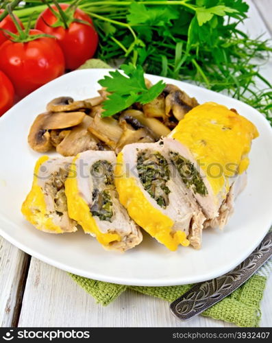Roll of chicken breast with spinach, mushrooms and cheese in a white plate with grilled mushrooms and parsley on a napkin, tomatoes, dill, tarragon on a wooden boards background