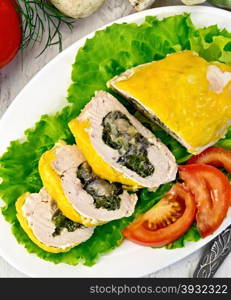 Roll of chicken breast with spinach, mushrooms and cheese on a green lettuce on a plate with slices of tomato, fork on the background of wooden boards