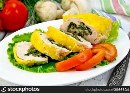 Roll of chicken breast with spinach, mushrooms and cheese on green salad in a white plate with slices of tomato, a napkin on a wooden boards background