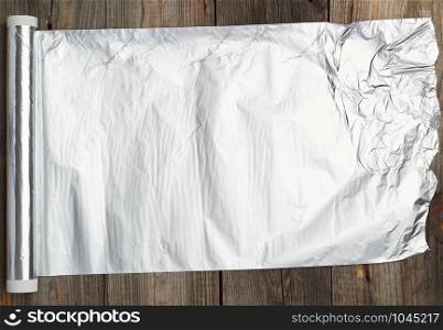 roll of gray foil for baking and packaging food on a wooden background, torn edge