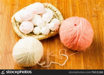 roll of white and pink soft knitting yarn and wattled plate with zephyr on wooden background